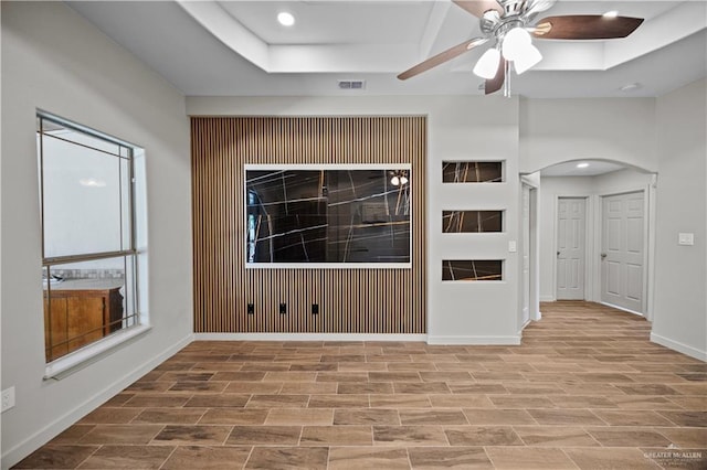 unfurnished room featuring a ceiling fan, wood finished floors, baseboards, a raised ceiling, and arched walkways