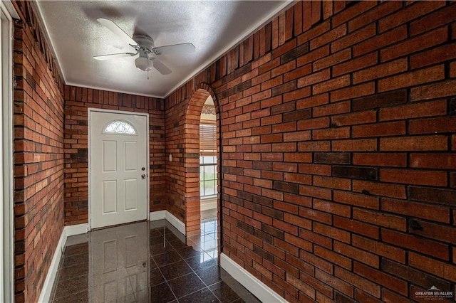 foyer entrance with ceiling fan, ornamental molding, a textured ceiling, and brick wall