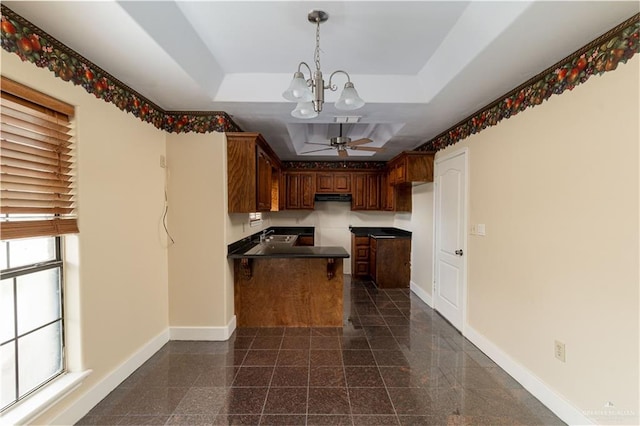 kitchen featuring ceiling fan with notable chandelier, a raised ceiling, kitchen peninsula, and hanging light fixtures