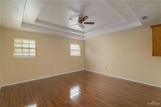 empty room with dark hardwood / wood-style flooring, a tray ceiling, and ceiling fan