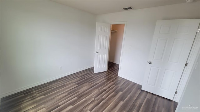 unfurnished bedroom featuring a walk in closet, a closet, and dark hardwood / wood-style flooring