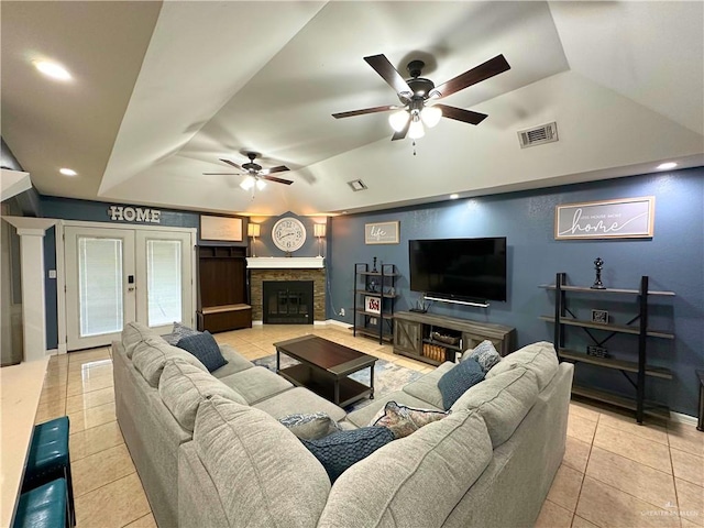 tiled living room with a stone fireplace, ceiling fan, french doors, and vaulted ceiling