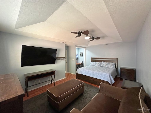 bedroom with ceiling fan, wood-type flooring, a textured ceiling, and a tray ceiling