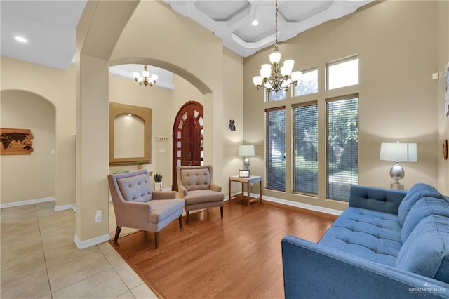 interior space featuring beam ceiling, a high ceiling, coffered ceiling, light hardwood / wood-style floors, and a chandelier