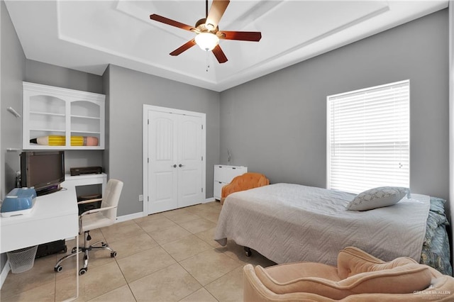 bedroom featuring light tile patterned floors, a closet, a raised ceiling, and ceiling fan