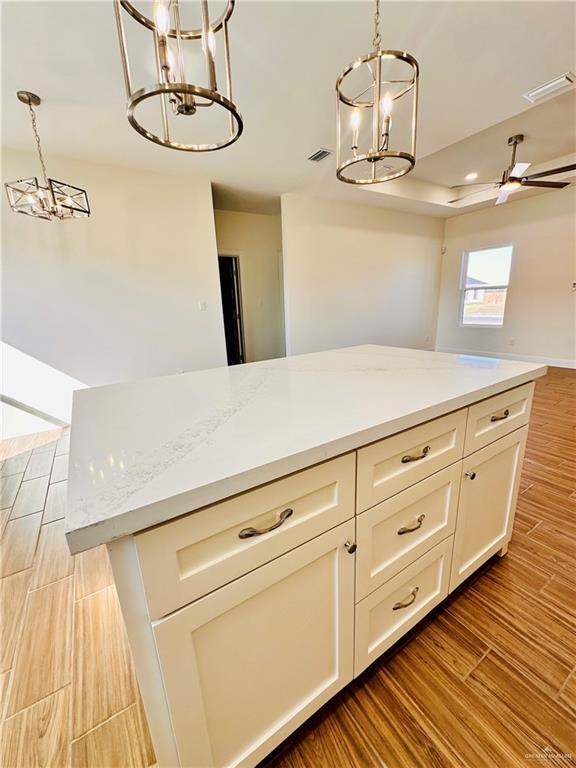 kitchen featuring hanging light fixtures, hardwood / wood-style flooring, ceiling fan, light stone countertops, and a kitchen island