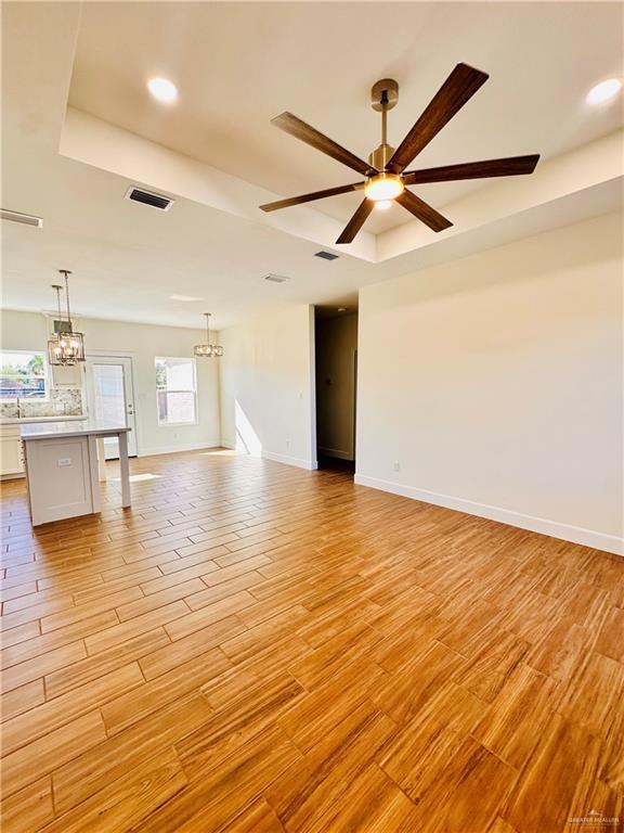 unfurnished living room featuring ceiling fan with notable chandelier, light hardwood / wood-style floors, and a tray ceiling