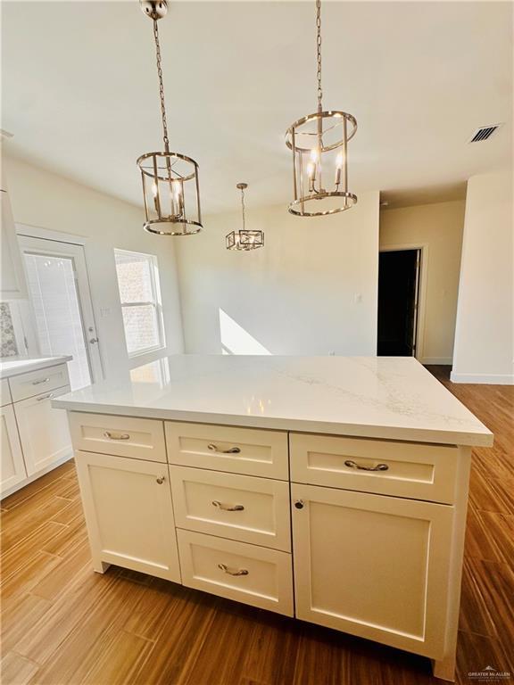 kitchen featuring wood-type flooring, a center island, decorative light fixtures, and light stone counters