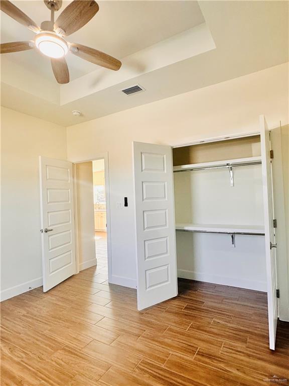 unfurnished bedroom featuring ceiling fan, a raised ceiling, wood-type flooring, and a closet