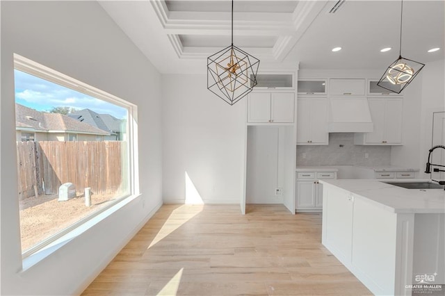 kitchen with white cabinetry, sink, hanging light fixtures, light stone counters, and custom exhaust hood