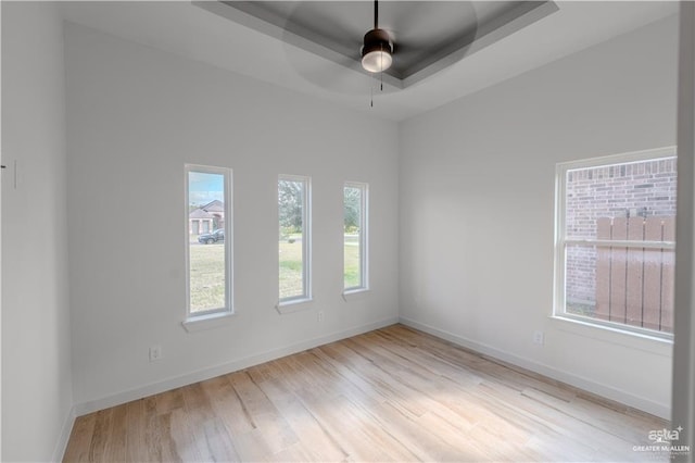 unfurnished room with ceiling fan, light wood-type flooring, and a tray ceiling