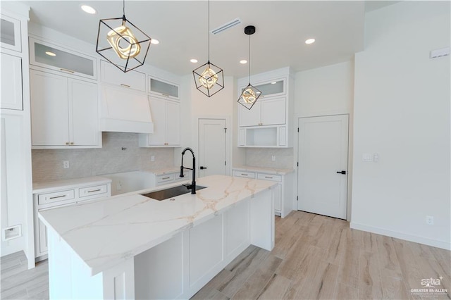 kitchen featuring white cabinets, light stone counters, a center island with sink, and sink