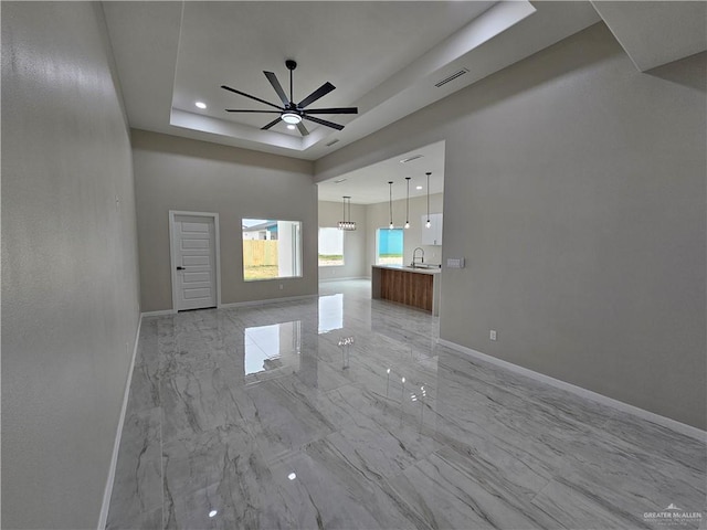 unfurnished living room featuring a tray ceiling, ceiling fan, and sink