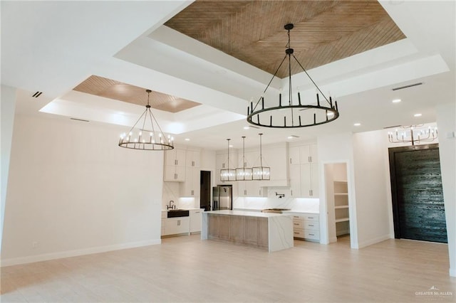 kitchen with hanging light fixtures, a tray ceiling, a spacious island, and white cabinetry