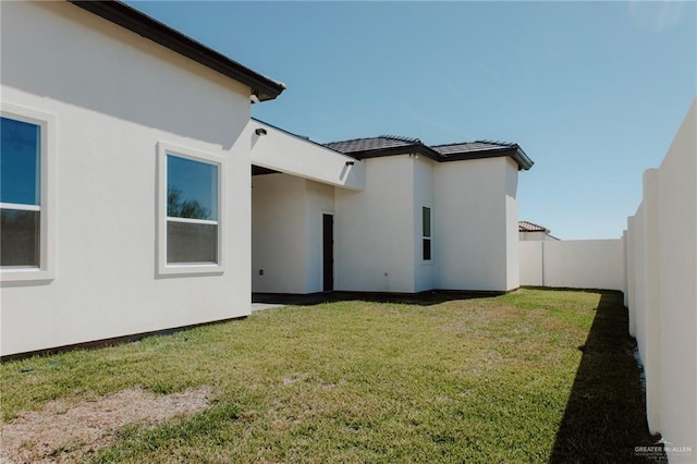 rear view of property featuring a fenced backyard, a lawn, and stucco siding