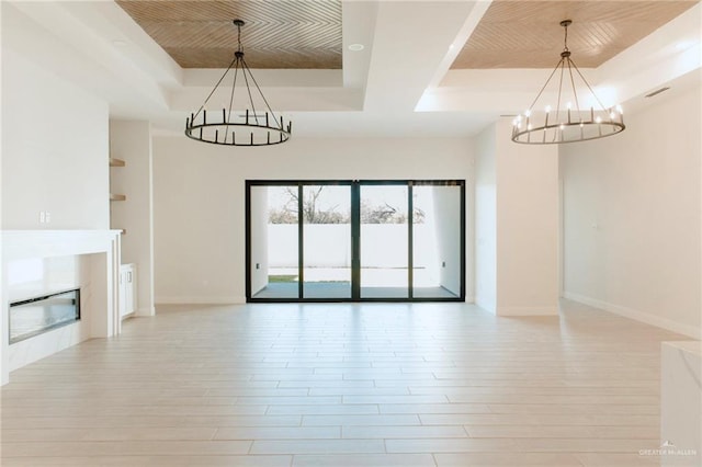 unfurnished living room featuring a chandelier, visible vents, light wood-style floors, a tray ceiling, and a glass covered fireplace