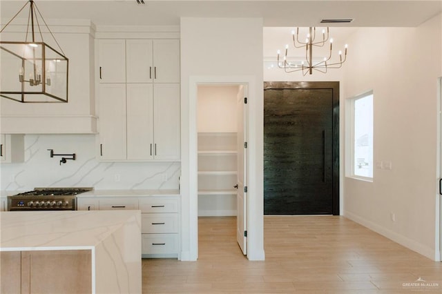 kitchen featuring pendant lighting, light wood finished floors, light stone countertops, and white cabinets