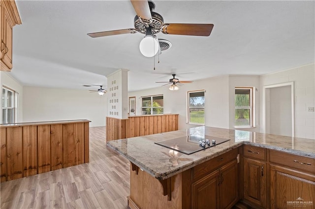 kitchen featuring light stone counters, a center island, light wood-type flooring, a kitchen breakfast bar, and black electric stovetop