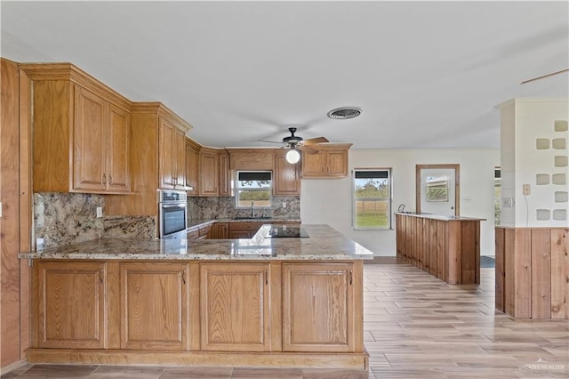 kitchen featuring sink, oven, ceiling fan, kitchen peninsula, and light stone countertops