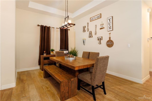 dining room with baseboards, a tray ceiling, and light wood-style floors