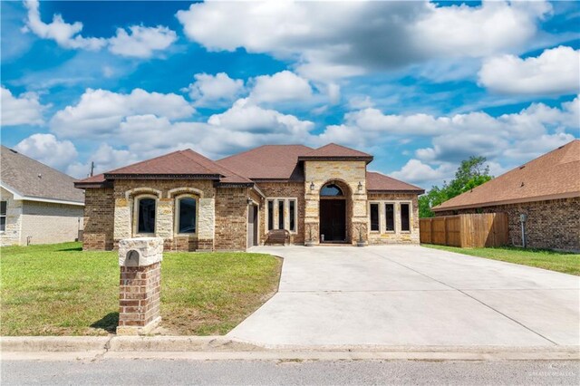 mediterranean / spanish house featuring driveway, stone siding, fence, brick siding, and a front yard