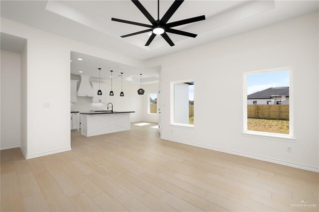 kitchen with premium range hood, pendant lighting, white cabinetry, sink, and a center island with sink