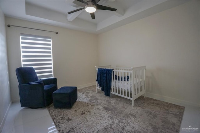 bedroom featuring a tray ceiling, baseboards, a crib, and a ceiling fan