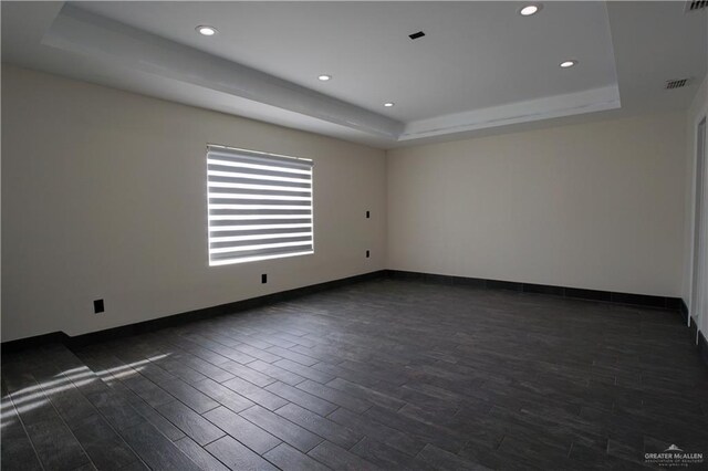 spare room with visible vents, a raised ceiling, dark wood-type flooring, and baseboards