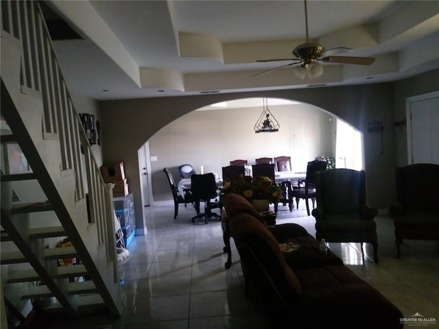 living room with ceiling fan with notable chandelier and a tray ceiling