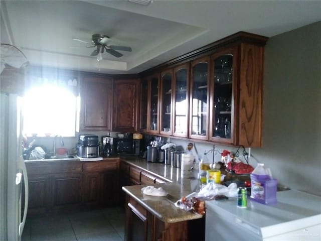 kitchen with ceiling fan, sink, a raised ceiling, white refrigerator, and kitchen peninsula