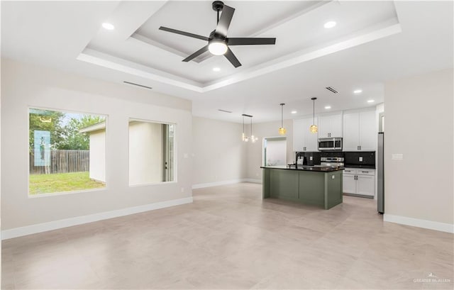 kitchen featuring pendant lighting, a raised ceiling, appliances with stainless steel finishes, white cabinetry, and an island with sink