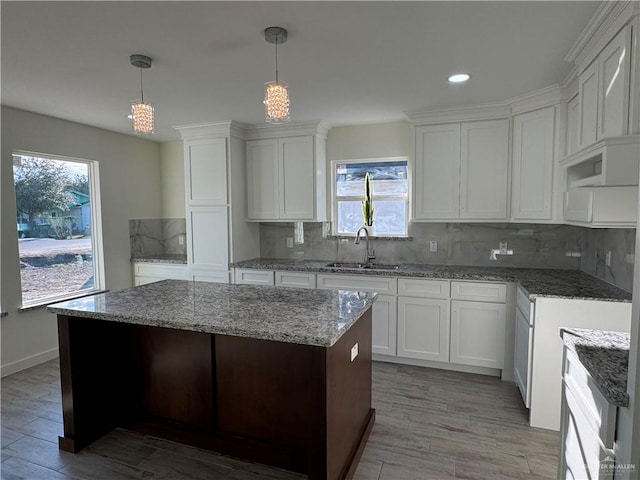 kitchen with a kitchen island, pendant lighting, white cabinetry, sink, and decorative backsplash