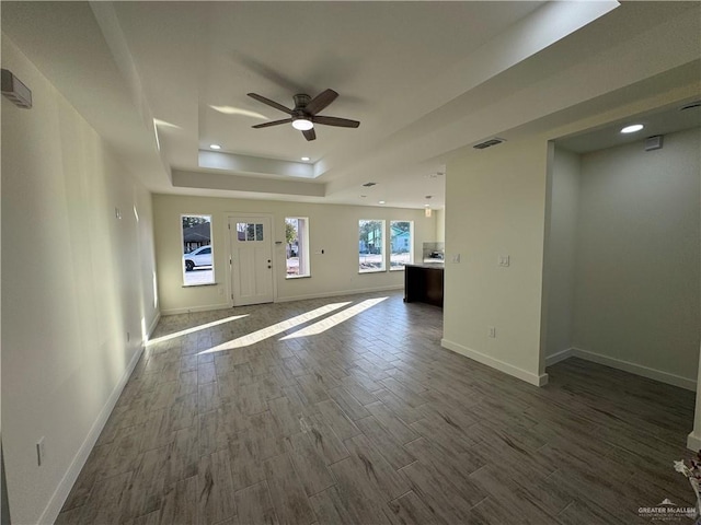 unfurnished living room with ceiling fan and a tray ceiling