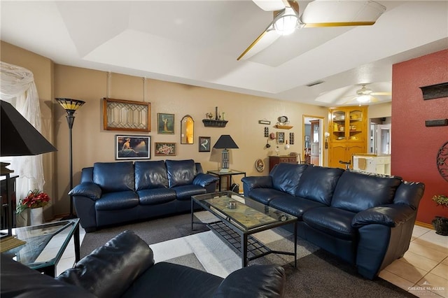 tiled living room with a tray ceiling and ceiling fan