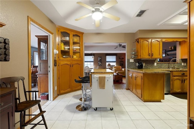 kitchen featuring a breakfast bar, a center island, sink, decorative backsplash, and light tile patterned floors