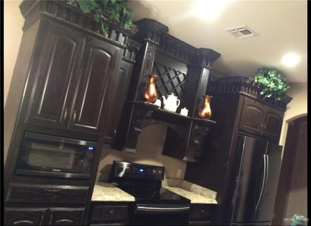 kitchen featuring visible vents, light stone countertops, dark brown cabinetry, freestanding refrigerator, and black electric range oven