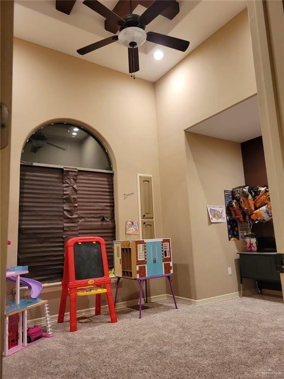 rec room featuring a towering ceiling, a ceiling fan, baseboards, and carpet floors