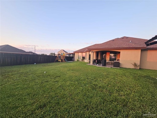 yard at dusk with a patio, fence, and a playground