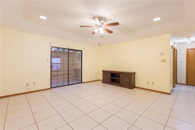 tiled empty room featuring ceiling fan and a tray ceiling