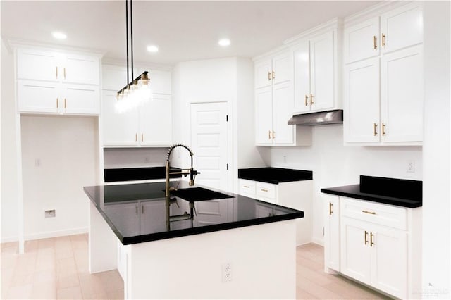 2221 N Woody St, Edinburg, TX 78541 - kitchen with under cabinet range hood, dark countertops, a kitchen island with sink, white cabinetry, and recessed lighting