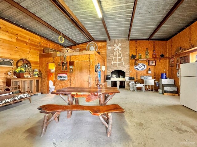 dining area featuring vaulted ceiling with beams, concrete floors, a stone fireplace, and wooden walls