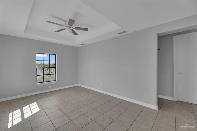 tiled empty room featuring ceiling fan and a tray ceiling