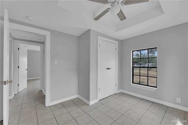 tiled empty room featuring a raised ceiling and ceiling fan