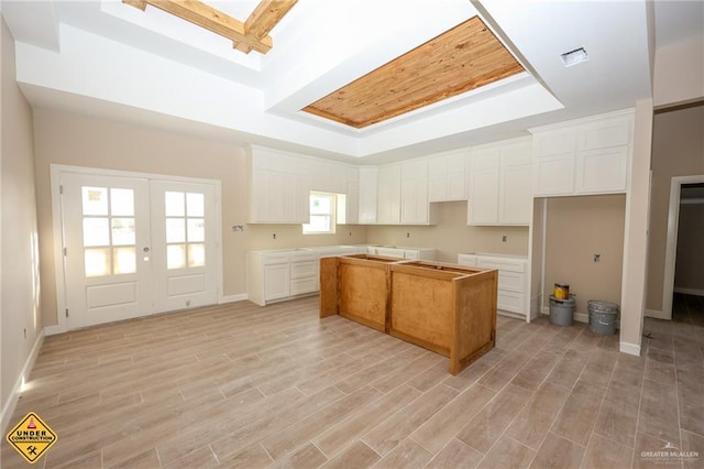 kitchen with a center island, white cabinetry, a tray ceiling, light wood-type flooring, and french doors