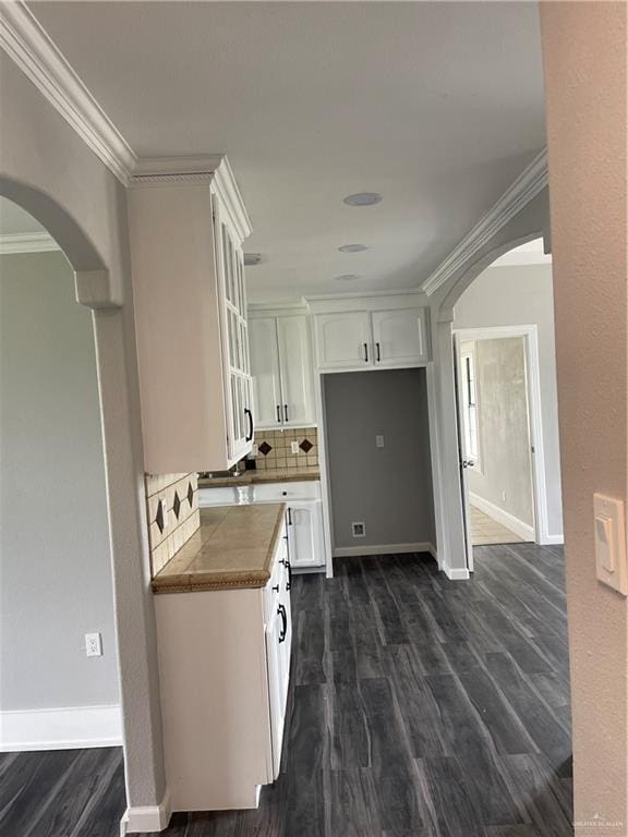 kitchen featuring white cabinets, decorative backsplash, ornamental molding, and dark wood-type flooring