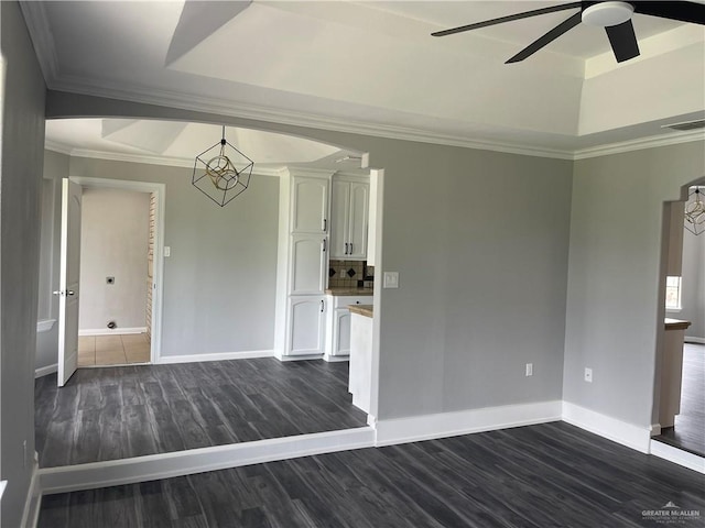 spare room with a tray ceiling, dark hardwood / wood-style flooring, ceiling fan with notable chandelier, and ornamental molding