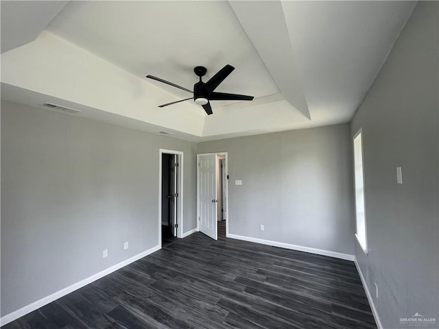 unfurnished room with a raised ceiling, ceiling fan, and dark hardwood / wood-style flooring