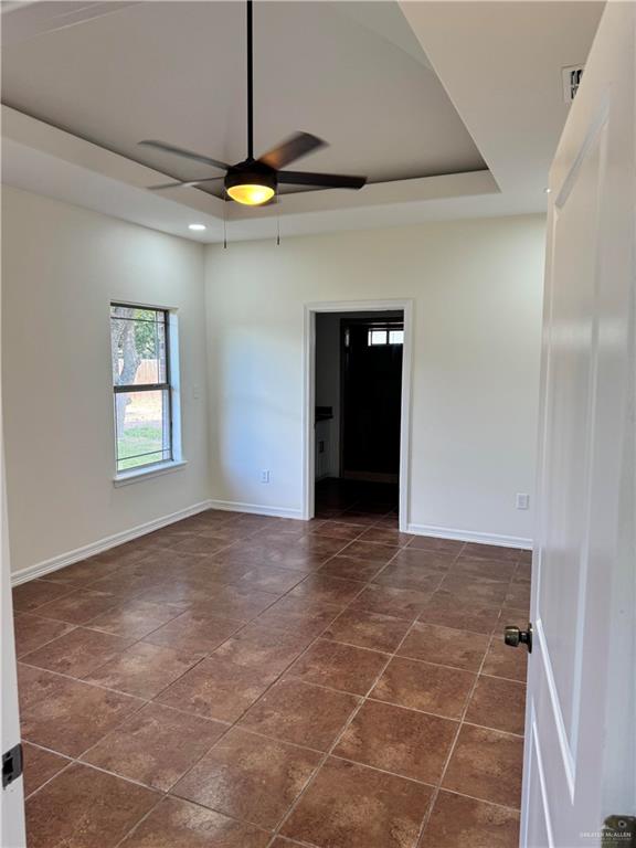 spare room featuring dark tile patterned floors, ceiling fan, and a tray ceiling