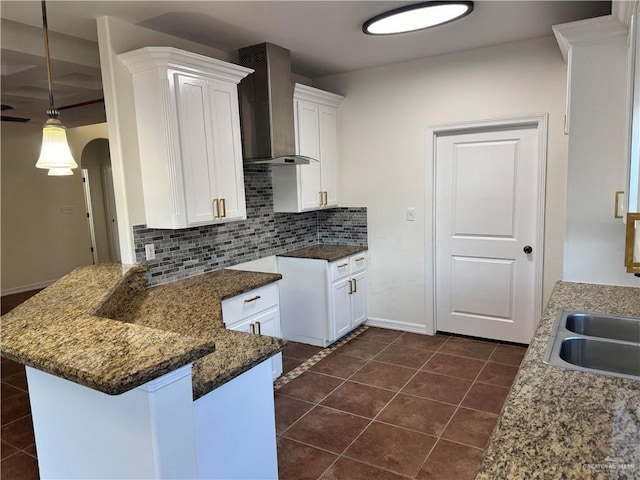 kitchen featuring white cabinets, dark tile patterned flooring, wall chimney exhaust hood, tasteful backsplash, and kitchen peninsula