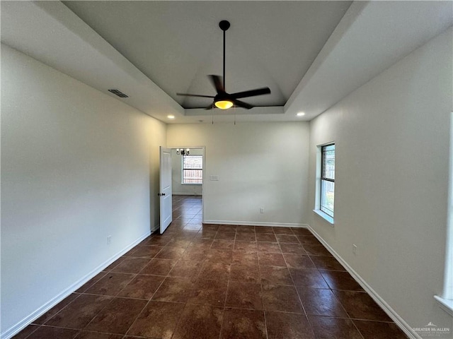 tiled empty room featuring a tray ceiling and ceiling fan